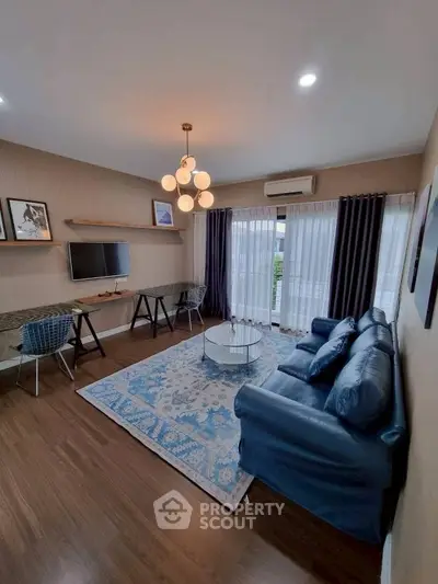 Modern living room with stylish decor, featuring a blue sofa, elegant lighting, and a cozy workspace.