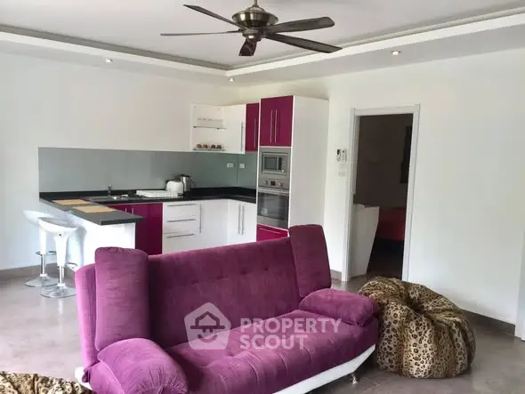 Modern open-layout living room with vibrant purple sofa and sleek kitchen area.