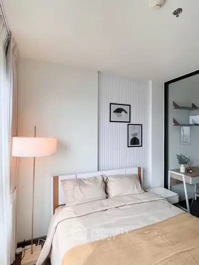 Modern bedroom with stylish decor and natural light, featuring a cozy bed and elegant lamp.