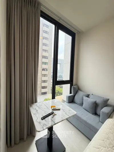 Modern living room with city view, featuring a cozy gray sofa and elegant marble table.