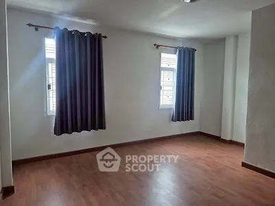 Spacious empty room with wooden flooring and large windows, perfect for customization.