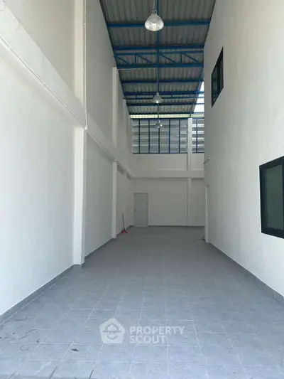 Spacious industrial-style interior with high ceiling and tiled floor, perfect for versatile use.
