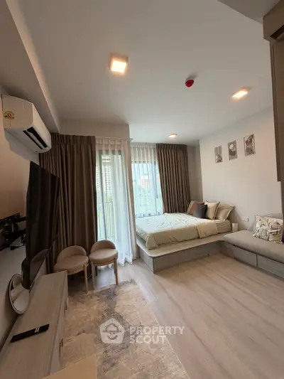 Modern studio apartment with cozy bed, stylish decor, and natural light from large windows.