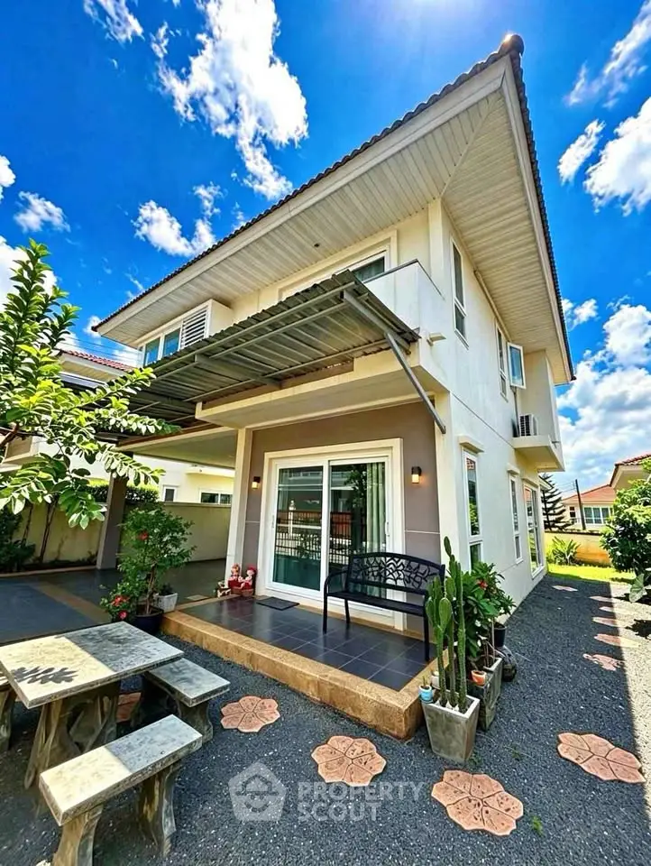 Charming two-story house with patio and lush garden under a bright blue sky.