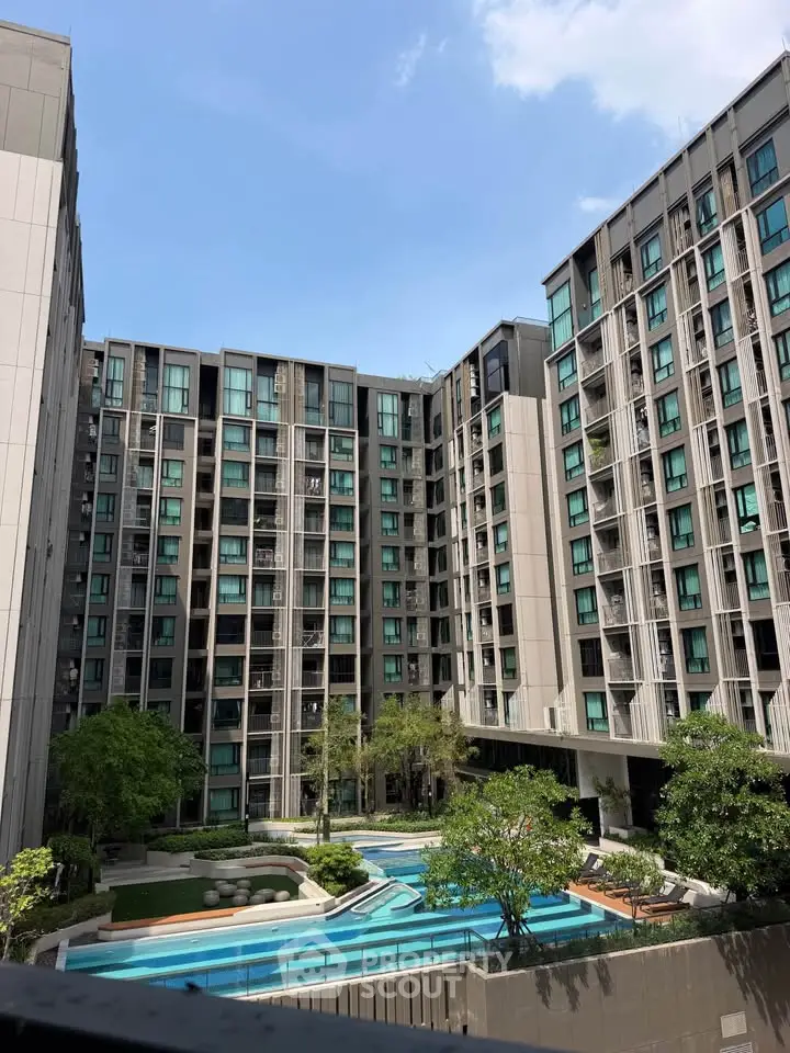 Modern apartment complex with pool and lush greenery under a clear blue sky.