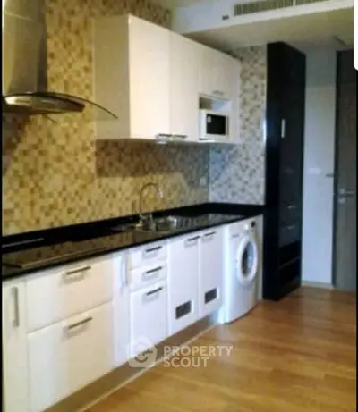 Modern kitchen with sleek cabinets, washing machine, and mosaic backsplash in a stylish apartment.