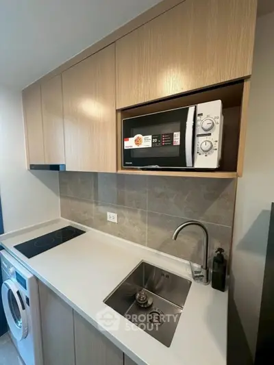 Modern kitchen with sleek cabinetry, built-in microwave, and compact washer in a stylish apartment.