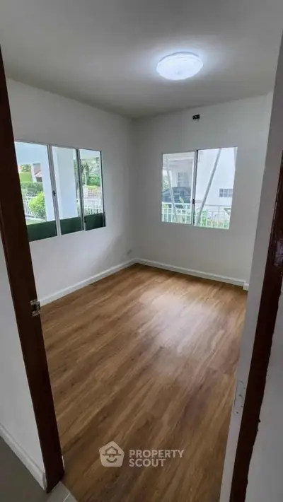 Bright empty room with wooden flooring and large windows in modern home.