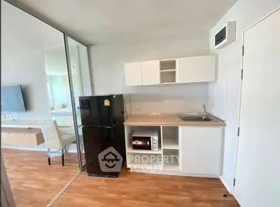 Modern compact kitchen with sleek cabinetry and black fridge in a bright apartment.