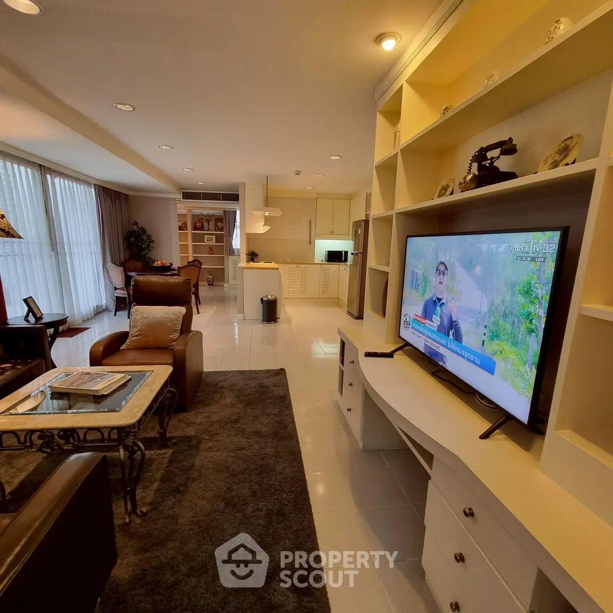 Spacious living room with modern decor and open kitchen layout, featuring a large TV and comfortable seating.