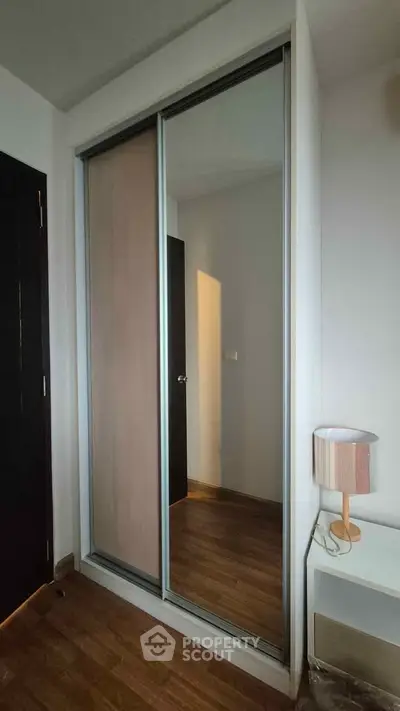 Modern bedroom with sliding mirror wardrobe and stylish lamp on wooden floor.