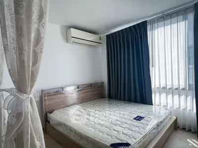 Bright bedroom with large window and air conditioning unit, featuring a new mattress.