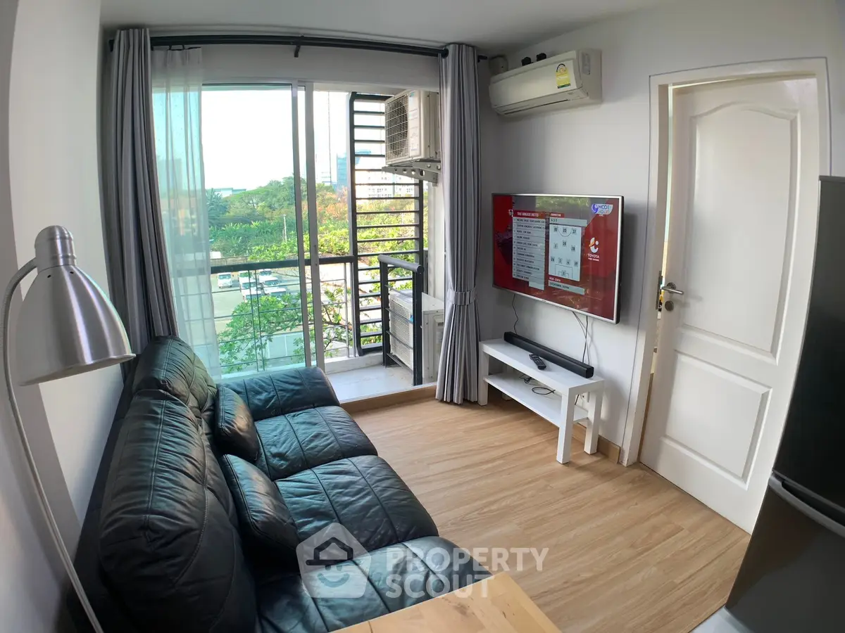 Modern living room with balcony view, black leather sofa, and wall-mounted TV in a cozy apartment.