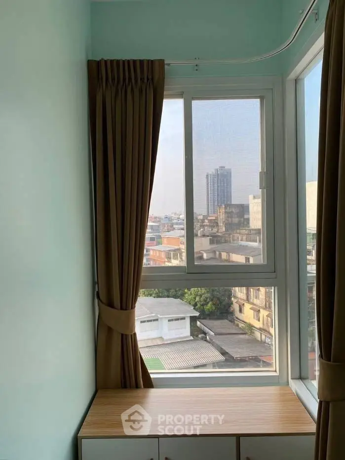 Bright room with large window offering city view, featuring modern curtains and a wooden cabinet.