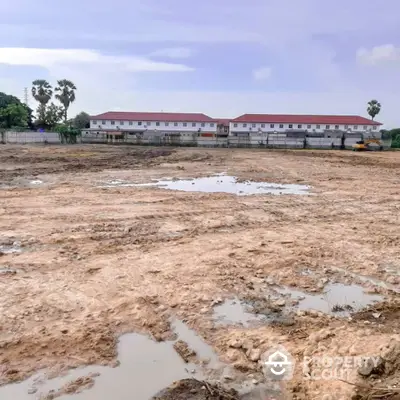 Expansive undeveloped land available for real estate development, showcasing potential with a backdrop of residential buildings under a clear sky.