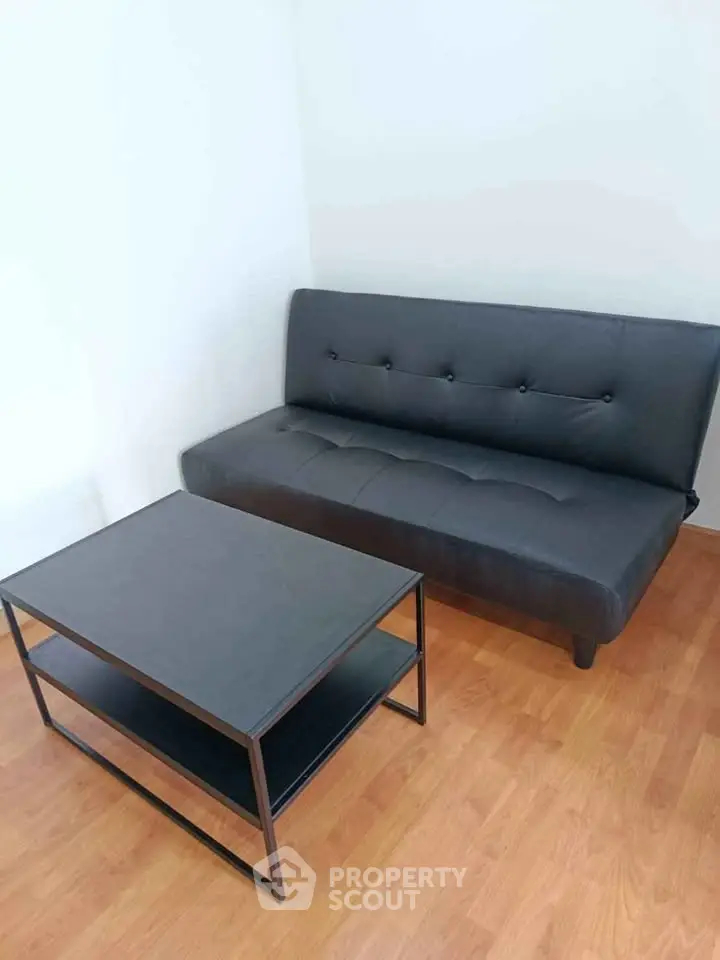 Modern minimalist living room with sleek black sofa and matching coffee table on wooden flooring.