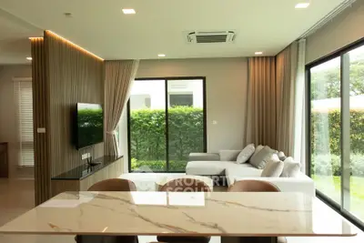 Modern living room with large windows and stylish furniture overlooking a lush garden.