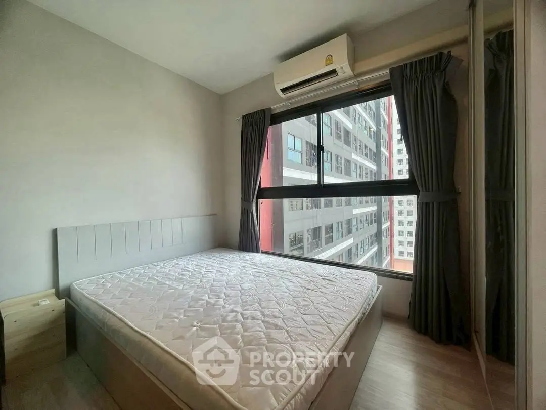 Cozy bedroom with large window and city view, featuring modern air conditioning unit.