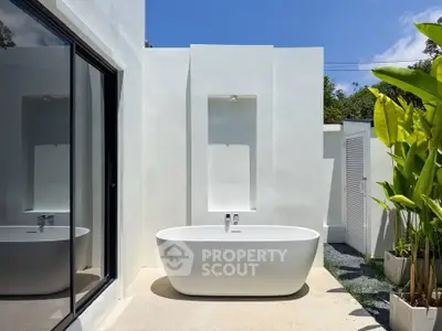 Luxurious outdoor bathroom with modern freestanding bathtub and lush greenery, perfect for relaxation.