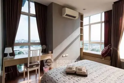 Bright bedroom with large windows and city view, featuring a cozy workspace and air conditioning.