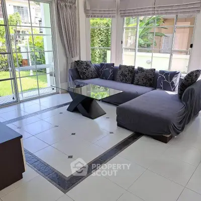 Spacious living room with modern decor and garden view, featuring a stylish sectional sofa and large windows.