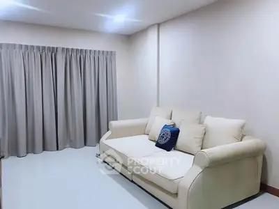 Spacious living room with elegant sofa and floor-to-ceiling curtains, perfect for relaxation.