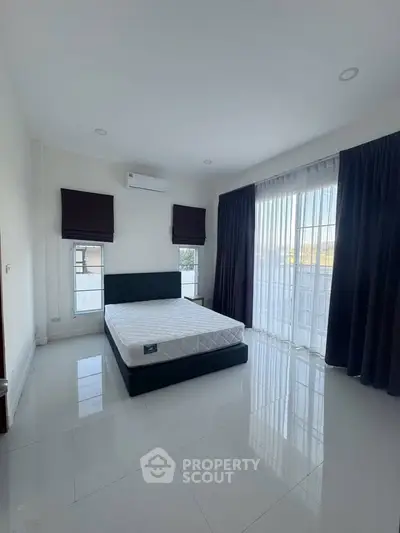 Spacious bedroom with large windows and modern decor, featuring a comfortable bed and elegant curtains.
