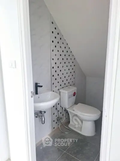 Compact bathroom with modern fixtures and stylish tile design under sloped ceiling.
