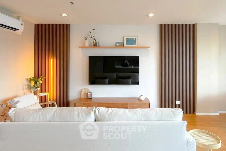 Modern living room with stylish decor and wall-mounted TV, featuring cozy seating and warm lighting.