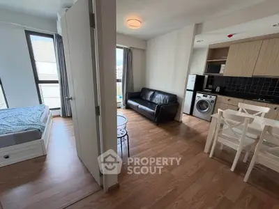 Modern studio apartment with open kitchen and cozy living area, featuring wooden flooring and ample natural light.