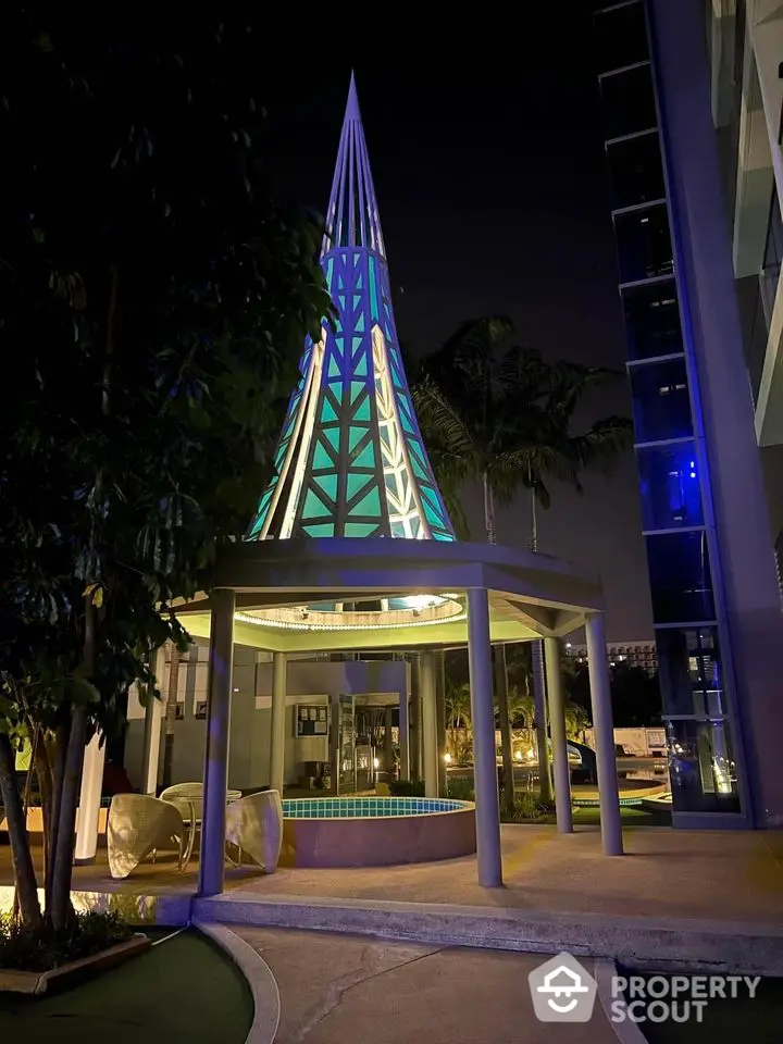 Stunning night view of modern architectural entrance with illuminated cone structure and lush greenery.