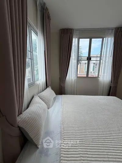 Cozy bedroom with large windows and elegant curtains, offering a bright and inviting atmosphere.