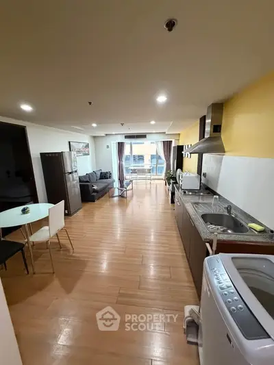 Spacious open-layout living room with modern kitchen and dining area, featuring wooden flooring and ample natural light.