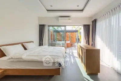 Spacious bedroom with large windows and modern decor, offering a serene garden view.