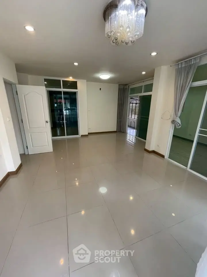 Spacious empty living room with modern chandelier and tiled flooring, ready for customization.