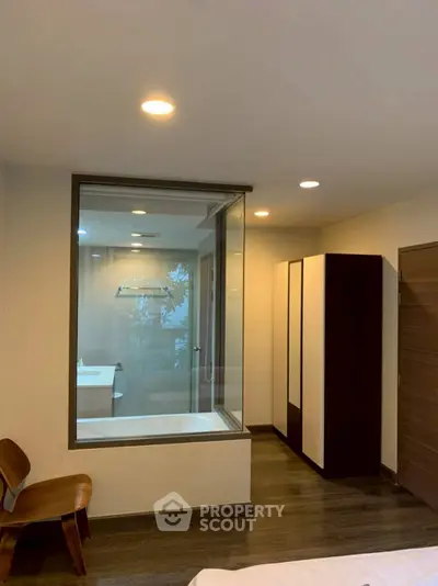 Modern bedroom with glass wall view into bathroom featuring a bathtub and sleek design.