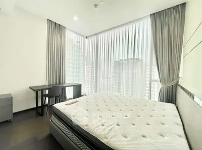 Spacious bedroom with large windows and modern furnishings in a high-rise apartment.