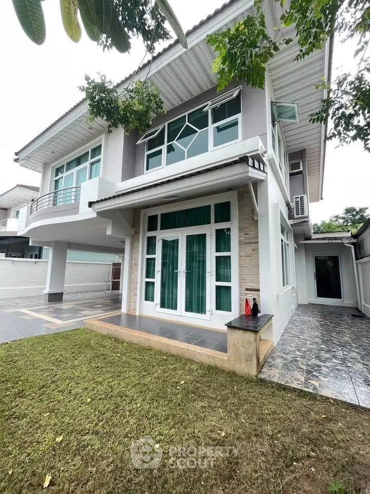 Stunning modern two-story house with large windows and lush green lawn in a serene neighborhood.