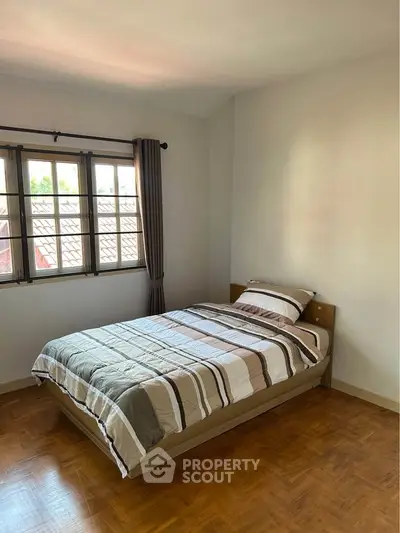 Cozy bedroom with wooden flooring and natural light from large window.