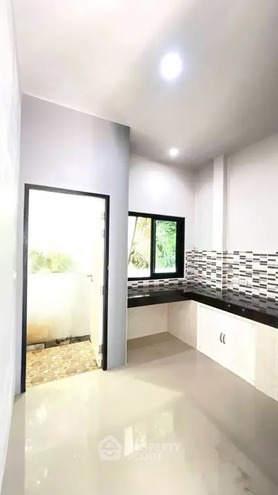 Modern kitchen with sleek black countertops and stylish backsplash, featuring an open layout and natural light.