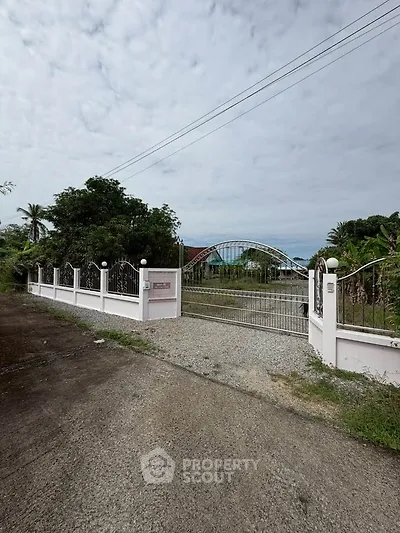 Charming gated property entrance with lush greenery and spacious driveway.