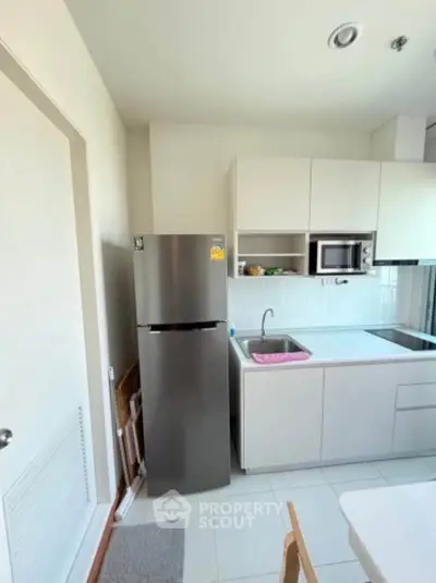 Modern kitchen with sleek appliances and minimalist design, featuring a stainless steel fridge and built-in microwave.