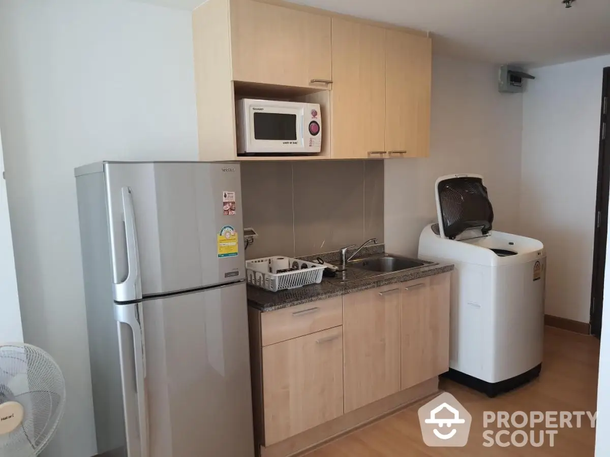 Modern kitchen with fridge, microwave, and washing machine in compact layout.