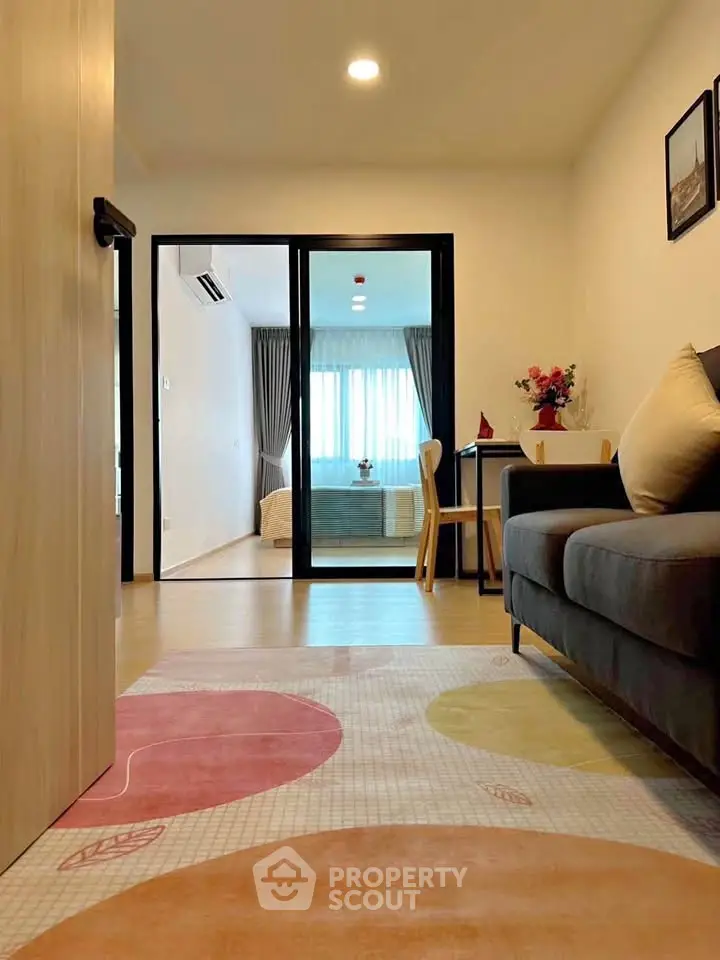 Modern living room with cozy sofa and view into a stylish bedroom through glass doors.