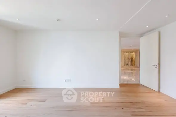 Spacious empty room with wooden flooring and open door leading to another area, ideal for customization.