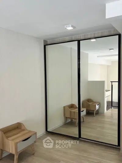 Modern bedroom with mirrored wardrobe and wooden nightstand, showcasing minimalist design.