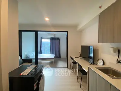 Modern studio apartment with open layout, featuring a cozy living area and bedroom separated by glass doors.