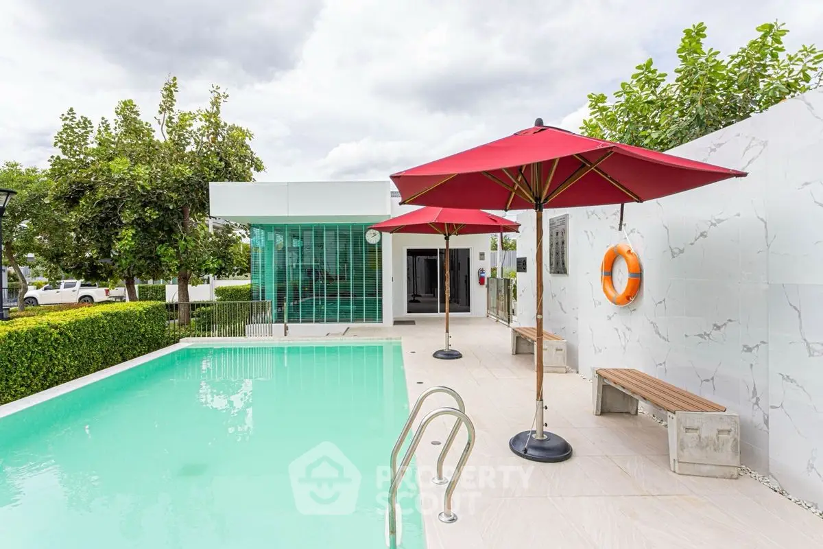 Luxurious modern poolside area with red umbrellas and lush greenery, perfect for relaxation and entertainment.