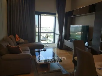 Modern living room with balcony and city view, featuring sleek furniture and large TV.