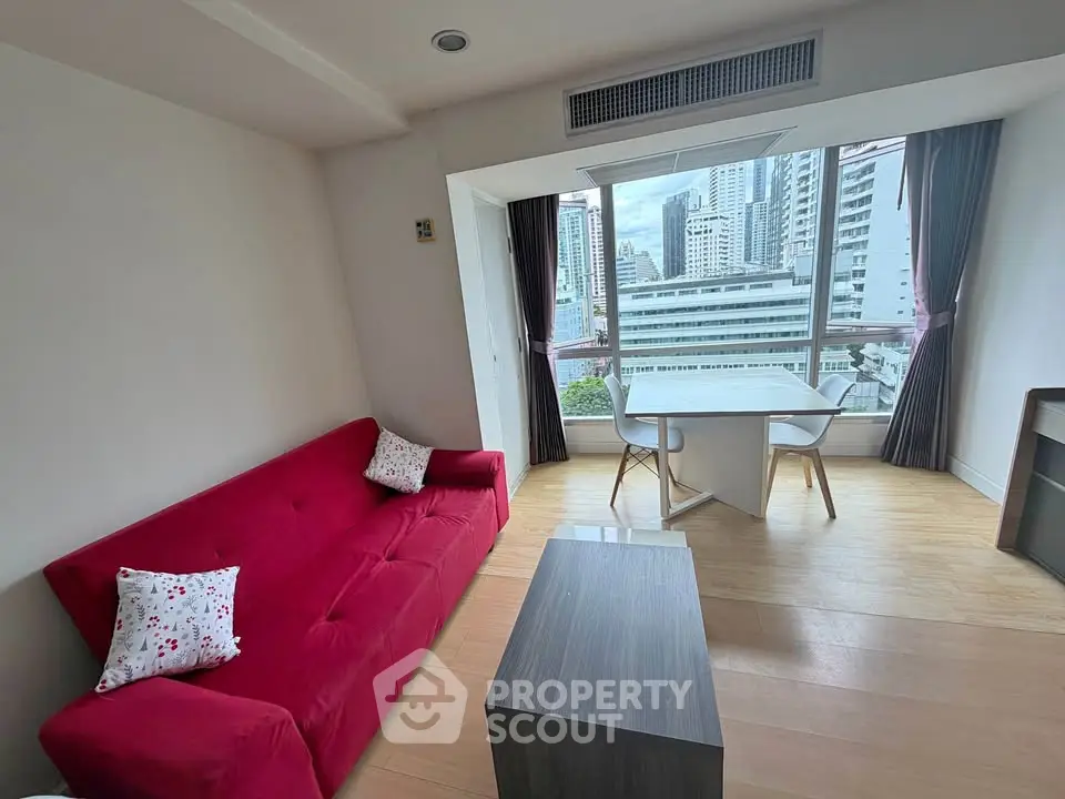 Modern living room with red sofa and city view, featuring a cozy dining area and large window.